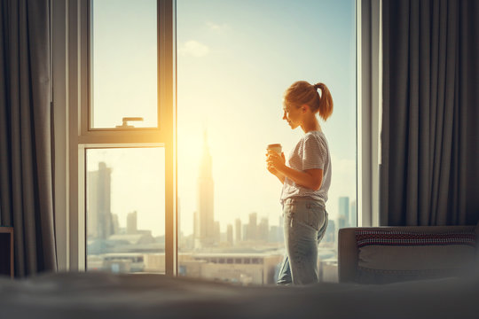 happy young woman drinks coffee in morning at window