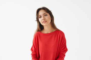 Horizontal isolated shot of serious beautiful young mixed race woman with brown hair posing in studio dressed in red oversize long sleeved top, looking at camera with calm facial expression