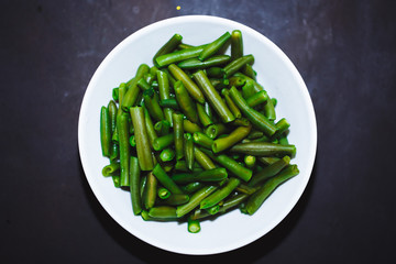 Cooked green beans in white plate on black background, Close up, top view. healthy food, proper nutrition.