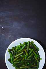 Cooked green beans in white plate on black background, Close up, top view. healthy food, proper nutrition, copy space.