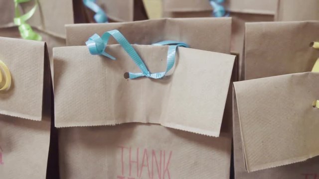 Slow motion. Birthday party favors in brown bags with colorful ribbons