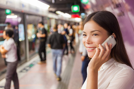 Businesswoman On Subway Metro Commute Public Transport Station Talking On The Phone While Walking To Arriving Train. Asian Woman Happy Using Mobile Cellphone App For Conversation.