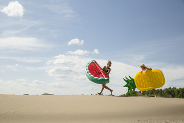 Girls chase each other across sand dunes with giant fruit