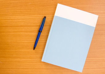 Hardcover book with ballpen  on wooden table, top view shot.