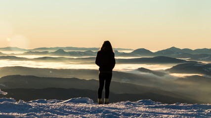 Young girl watching the sunrise from the top of Calimani mountains in Romania on a very cold winter morning.