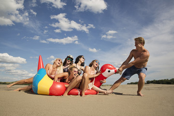 Boy pulls group of laughing girls on an inflatable parrot at the beach