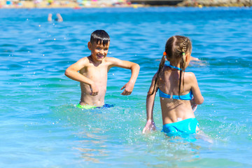 Obraz na płótnie Canvas Little boy and girl playing splashing sea water on beach holiday