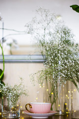 Pink vintage cup with tea on the cupboard near the mirror among the white dry flowers gypsophila. Home interior and still life