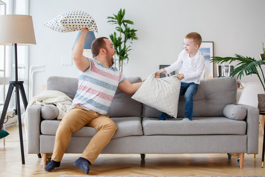 Photo of father fighting with son cushions on gray sofa