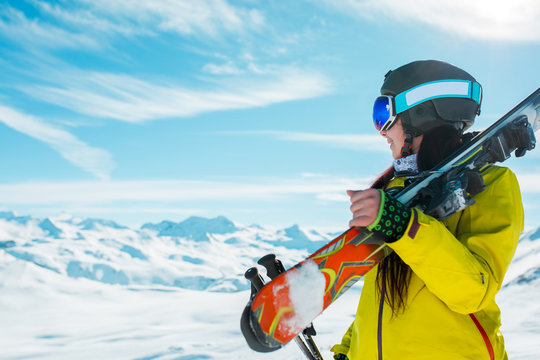 Photo of side view of sporty woman in helmet with skis on her shoulder against background of winter hills