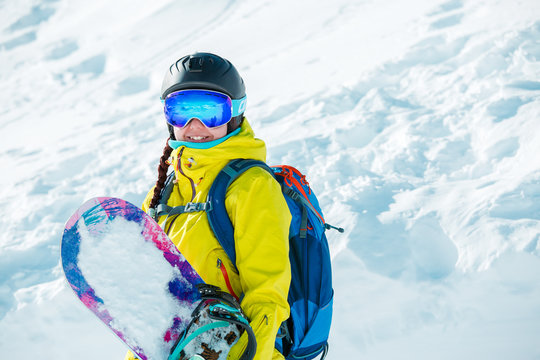 Picture of smiling woman in helmet and with snowboard on background of snowy landscape