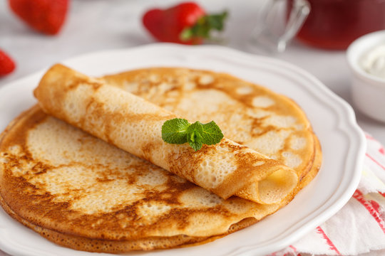 Thin hot pancakes with sour cream, jam and strawberries. Healthy traditional breakfast concept.