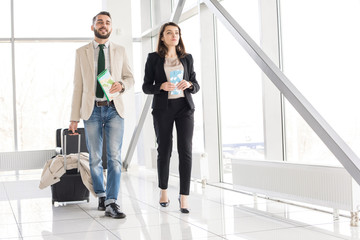 Full length portrait of modern couple holding airplane tickets and suitcase walking to gate in modern airport, copy space