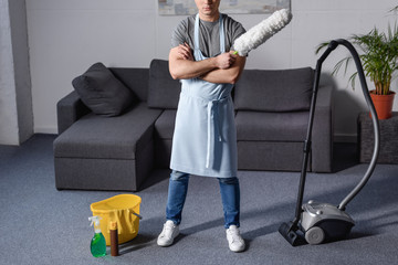cropped image of man standing and holding brush for cleaning dust in living room
