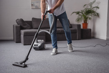 cropped image of man cleaning living room with vacuum cleaner