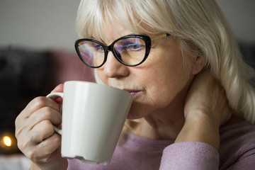 Pensive senior lady in glasses having cup of tea