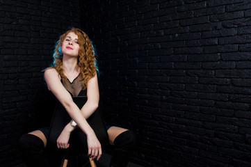 Curly hair girl at black clothes on studio against black brick wall.