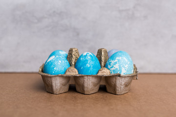 Painted eggs in egg carton on grey background