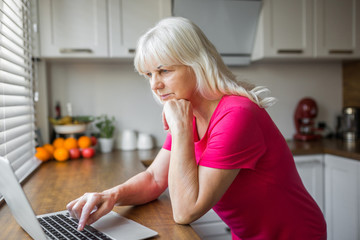 Senior lady using laptop on kitchen counter