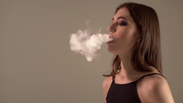 Girl with a vaporizer on a gray background vaping e-cigarette
