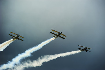 Group of vintage single engine propeller biplanes aircrafts flying with dark stormy sky background
