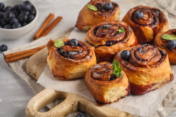 Homemade cinnamon buns with blueberries and cinnamon on a white wooden board