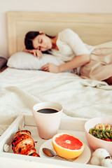 Beautiful young woman having healthy breakfast in bed. Reading book. Perfect morning quiet mood moment