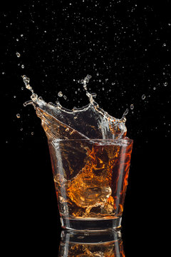 Glass of whiskey with splash isolated on black background