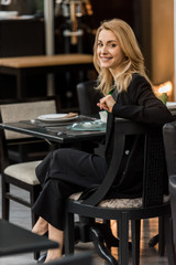 beautiful smiling woman looking at camera while sitting at table in cafe