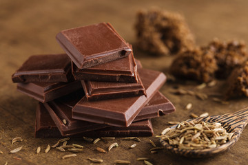 Chopped bitter chocolate in stack with cumin seeds on wooden background