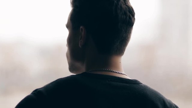 A young guy in a black sweater, stands with his back and looks back over his shoulder