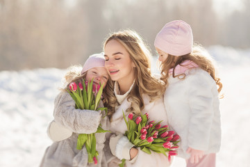 Obraz premium Portrait of young happy mother with a little daughters and tulips in the winter