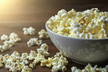 Popcorn in white bowl on wooden table in sunlight effect