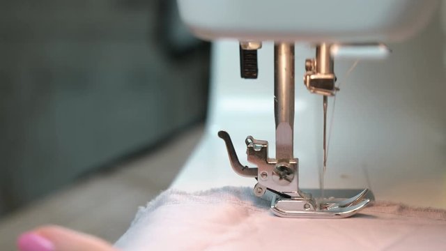 Woman sewing light fabric on a sewing machine close-up. Side view.