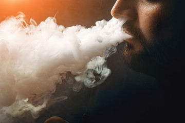 Man vape e-cigarette with e-liquid, close-up, breathes out large cloud of steam or vapor. Vaping...