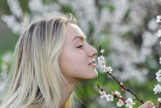 Closeup portrait of teenage girl inhales aroma of flowering apricot trees in the garden