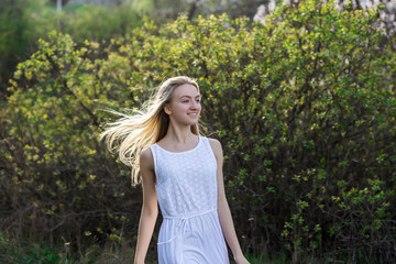 Teenage girl in white dress is running in the spring garden