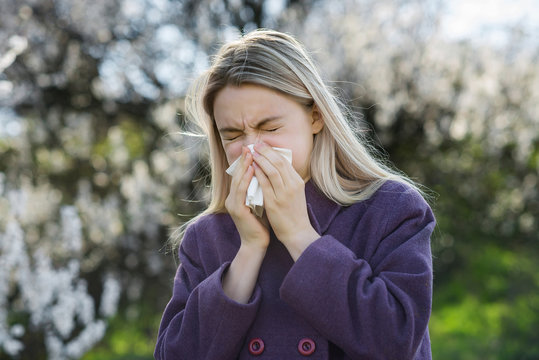 Girl blows his nose in a handkerchief against a backdrop of a blooming garden. The concept of an allergy