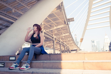 Fototapeta premium Young Asian woman is relaxing and drinking water after jogging in city.