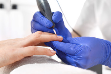 Manicure frezarkowe, kosmetyczka opracowuje paznokcie przy użyciu frezarki.