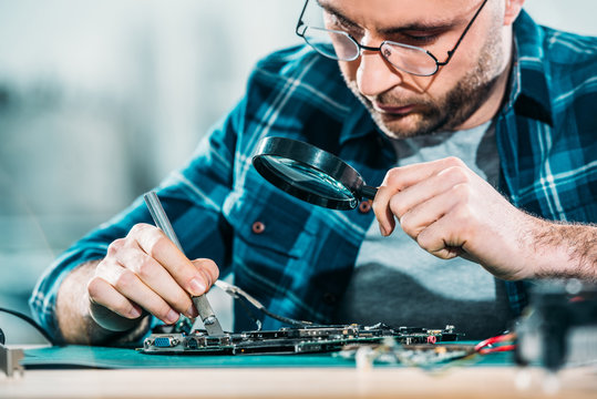 Engineer fixing circuit board looking through magnifying glass