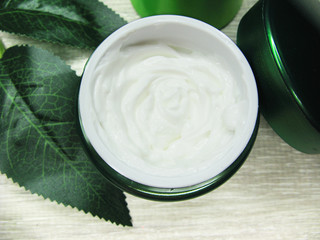 cosmetic cream for face care and green leaves