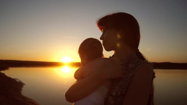 Mom holds a child in the arms of sunset at sunset. Slow motion.
