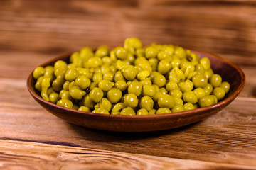 Ceramic plate with canned green pea on wooden table