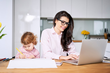 Working mother concept. Young woman working on laptop with her child from home