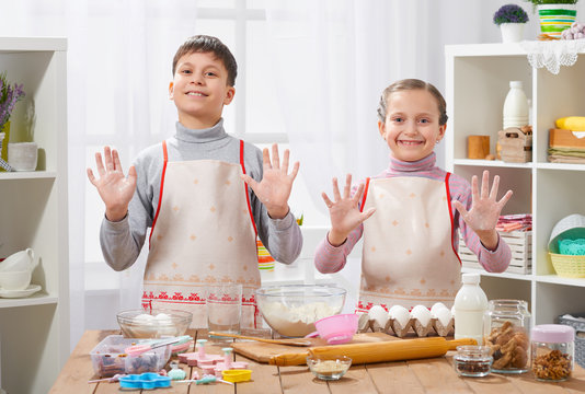 Child girl and boy cooking in home kitchen, showing hands with flour