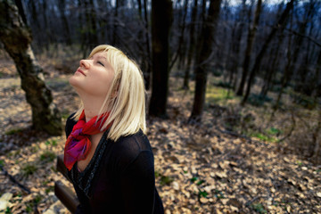 Fototapeta na wymiar Blonde woman with red scarf and black shirt in the forest looking up the sky. Springtime, outdoor portrait.