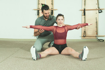 Yoga couple, Handsome male personal trainer with a beard helping young fitness girl to stretch her muscles after hard training workout, real people workout no posing, selective focus