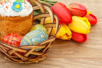 Easter cake and painted Easter eggs in wicker basket, red and yellow tulips