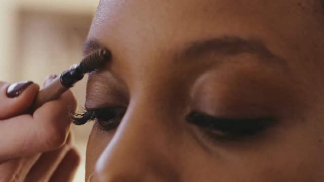 Makeup artist with brush combing eyebrows after plucking and correcting